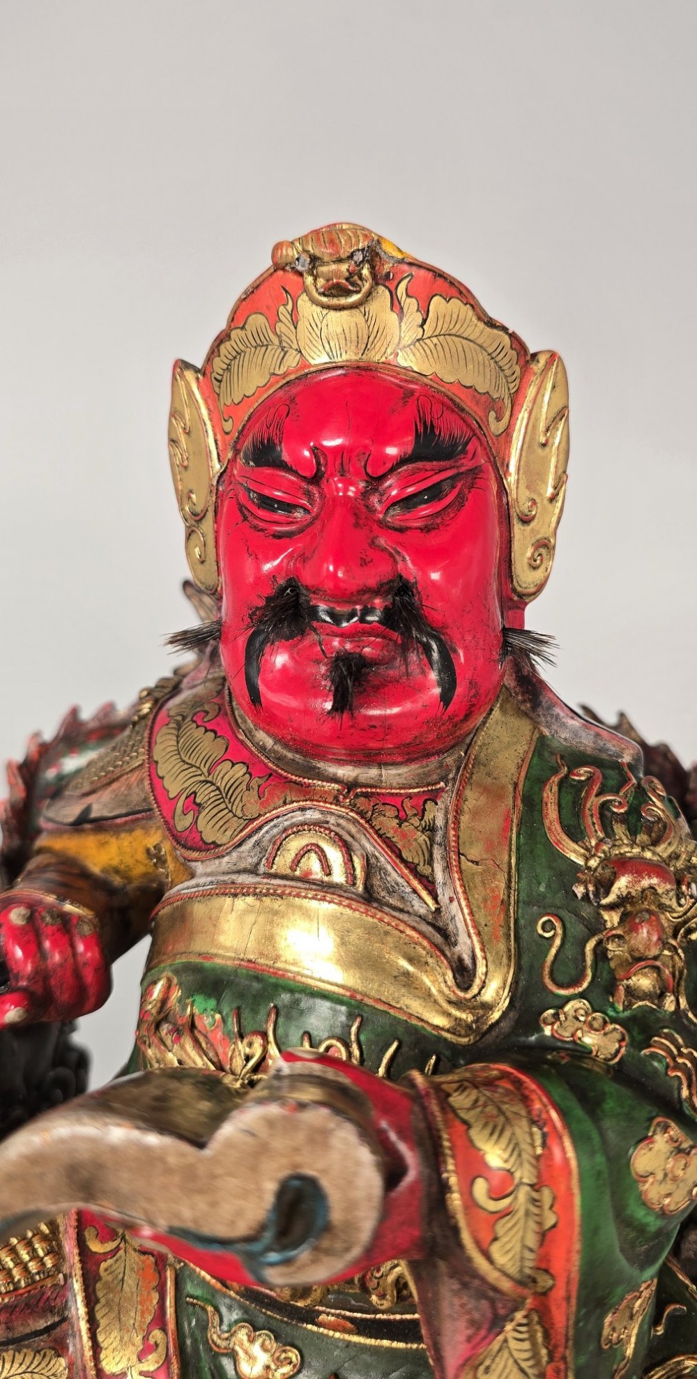 A carved Chinese lacquered wooden figure seated on a throne, rendered in bright red, green, and gold paint with intricate details. View XV