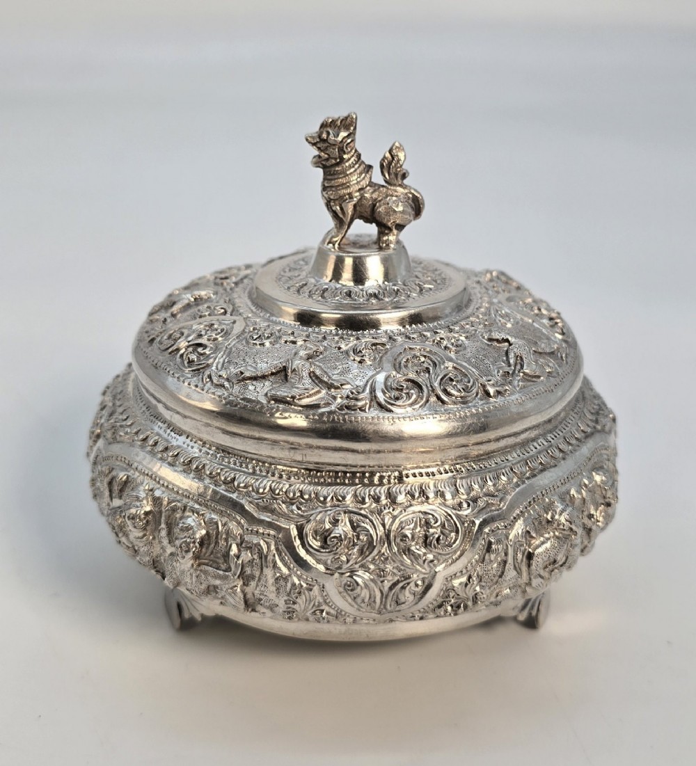 A circular Anglo-Indian chased silver jar featuring ornate scrollwork detailing and a small animal finial on the lid.