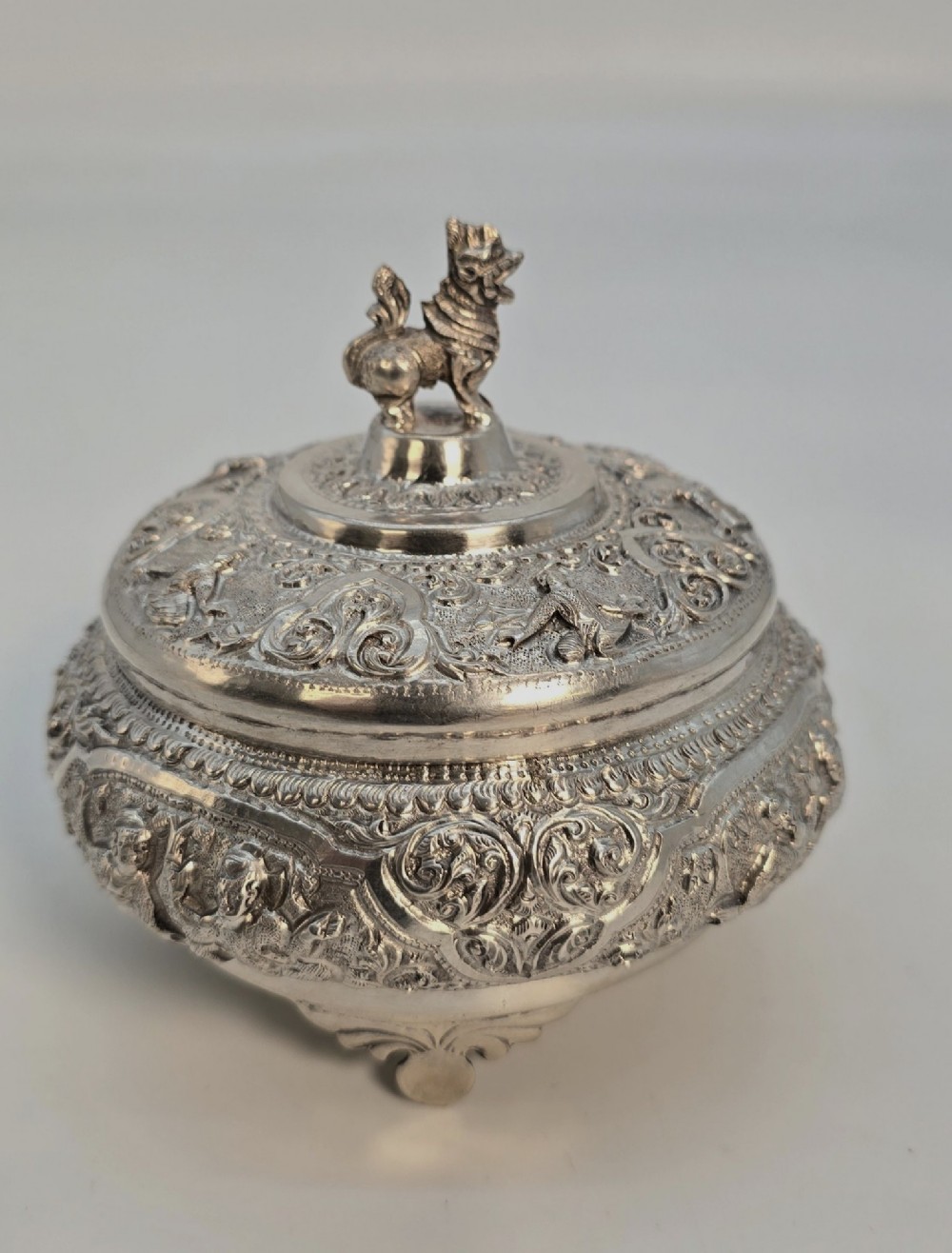 A circular Anglo-Indian chased silver jar featuring ornate scrollwork detailing and a small animal finial on the lid. View II