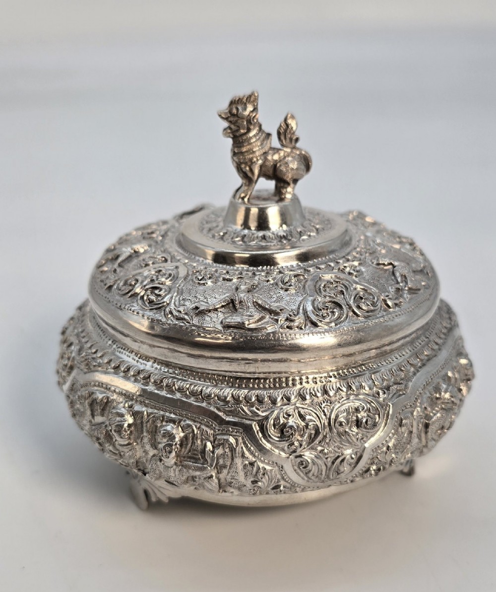 A circular Anglo-Indian chased silver jar featuring ornate scrollwork detailing and a small animal finial on the lid. View V