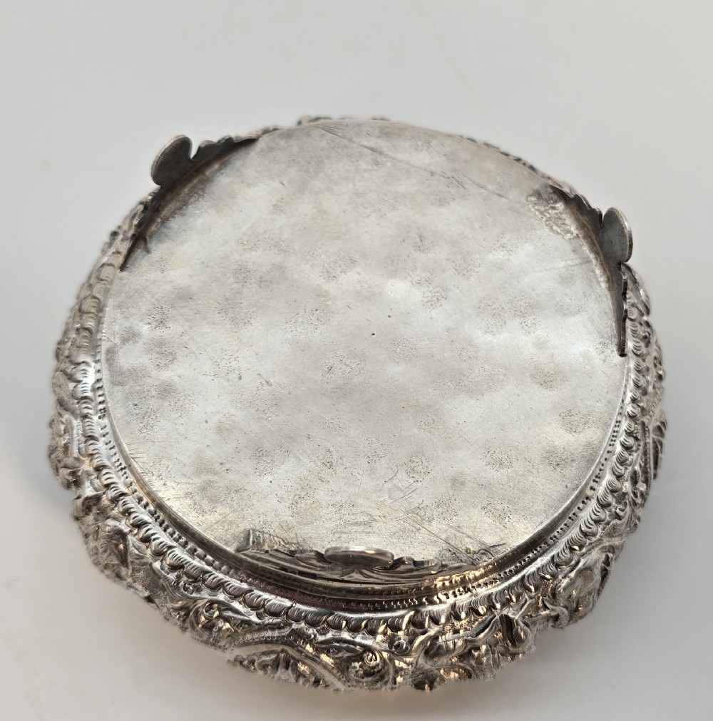 A circular Anglo-Indian chased silver jar featuring ornate scrollwork detailing and a small animal finial on the lid. View IX