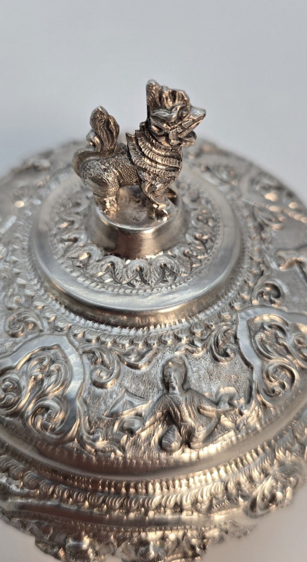 A circular Anglo-Indian chased silver jar featuring ornate scrollwork detailing and a small animal finial on the lid. View XII