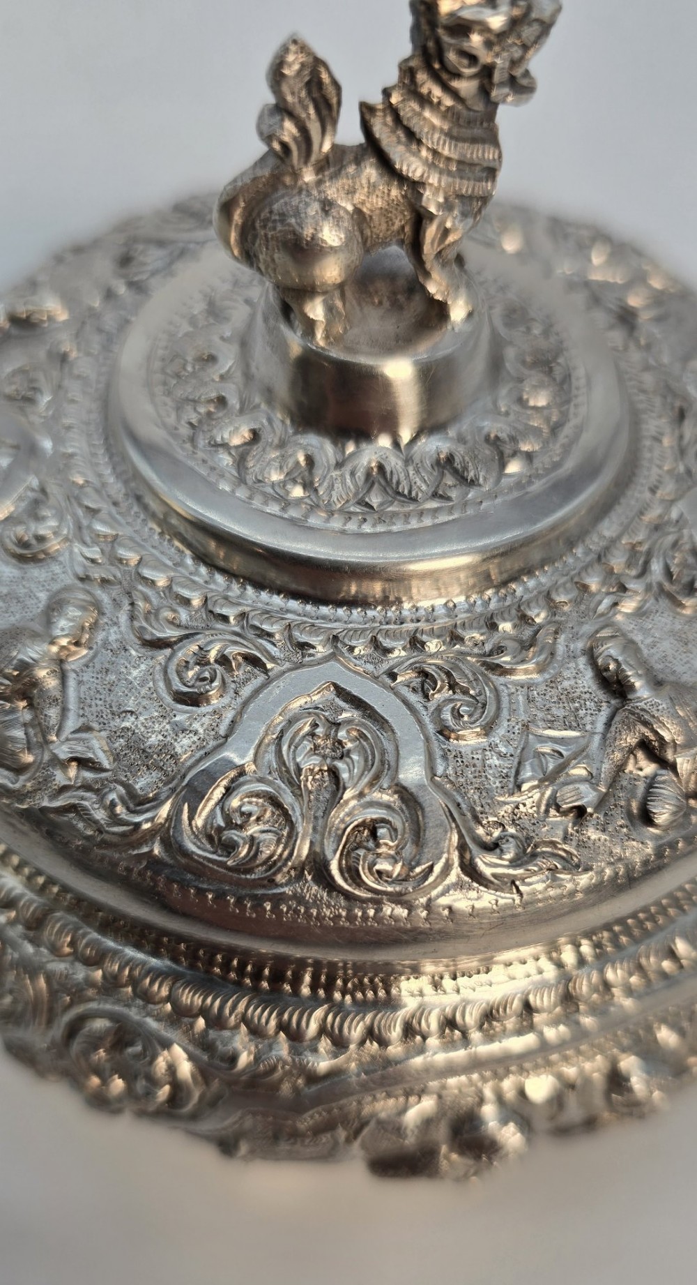 A circular Anglo-Indian chased silver jar featuring ornate scrollwork detailing and a small animal finial on the lid. View XIII