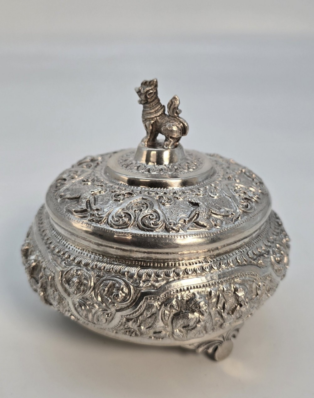 A circular Anglo-Indian chased silver jar featuring ornate scrollwork detailing and a small animal finial on the lid. View XIV