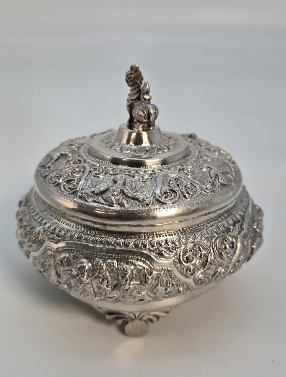 A circular Anglo-Indian chased silver jar featuring ornate scrollwork detailing and a small animal finial on the lid. View XV