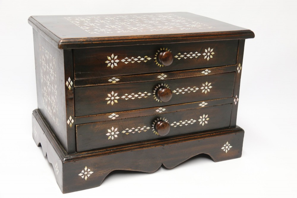 A dark hardwood tabletop chest featuring three drawers decorated with geometric bone inlay and turned wooden knobs.