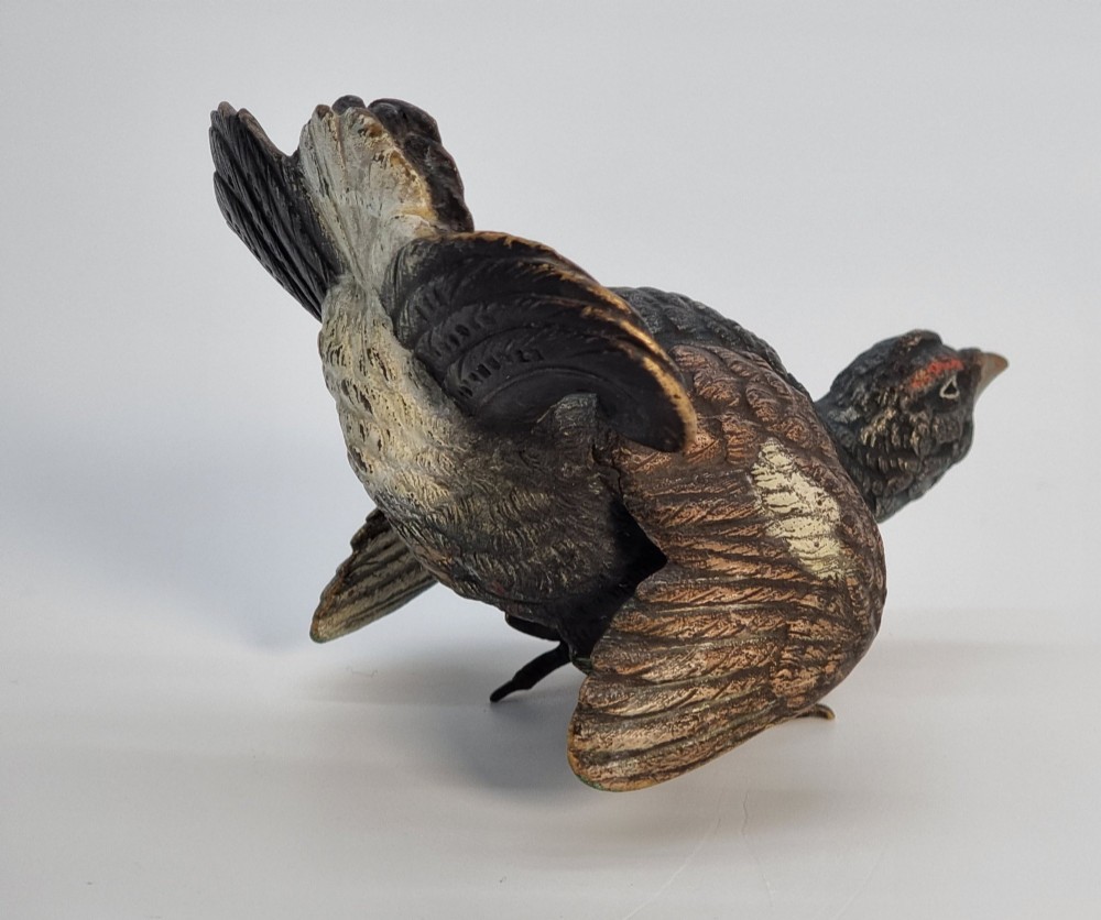 A cold painted bronze sculpture depicting a capercaillie in a display pose with textured dark brown feathers and red eye accents. View IV