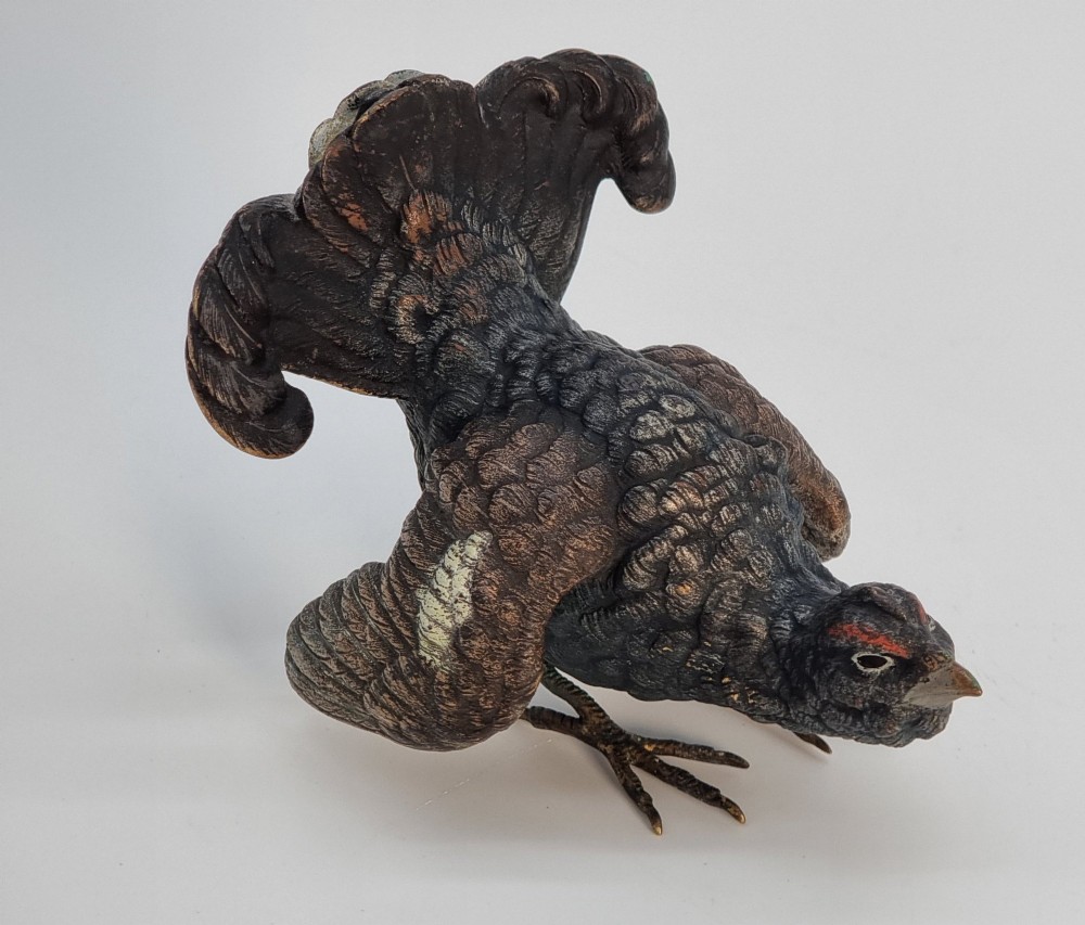 A cold painted bronze sculpture depicting a capercaillie in a display pose with textured dark brown feathers and red eye accents. View X