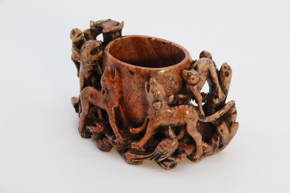 A cylindrical reddish-brown carved soapstone brush pot featuring sculpted animal figures in high relief surrounding an engraved vessel. View IV