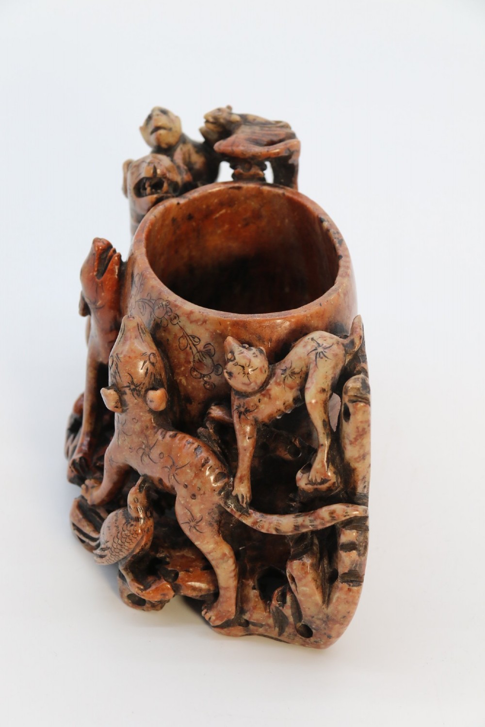 A cylindrical reddish-brown carved soapstone brush pot featuring sculpted animal figures in high relief surrounding an engraved vessel. View V