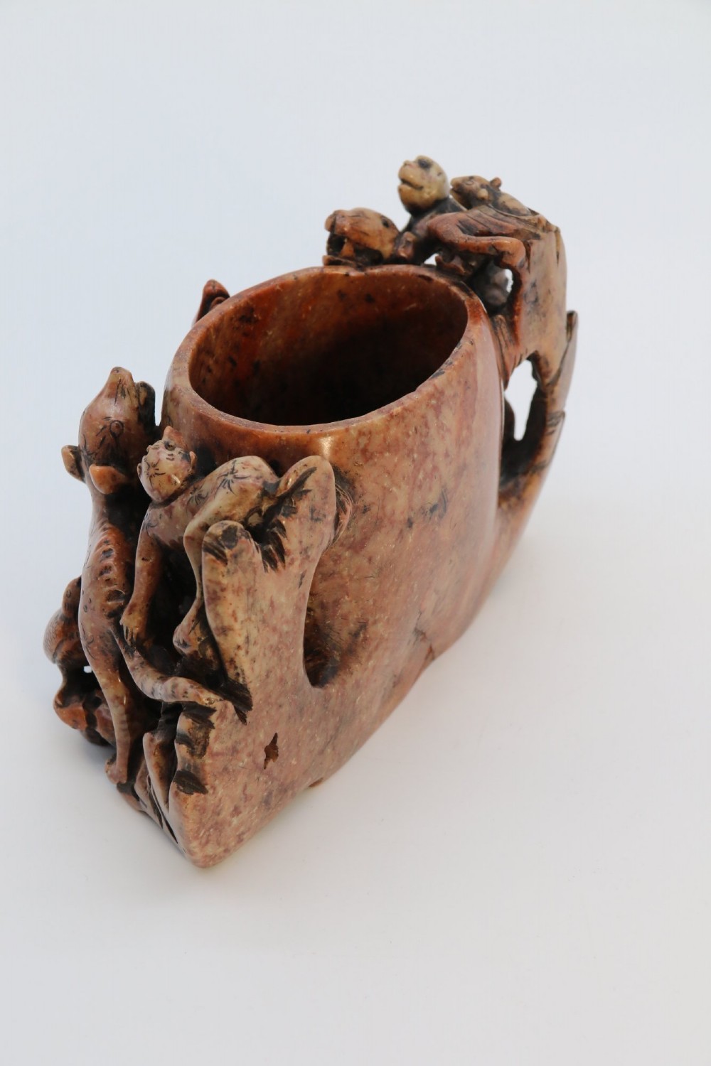 A cylindrical reddish-brown carved soapstone brush pot featuring sculpted animal figures in high relief surrounding an engraved vessel. View VI