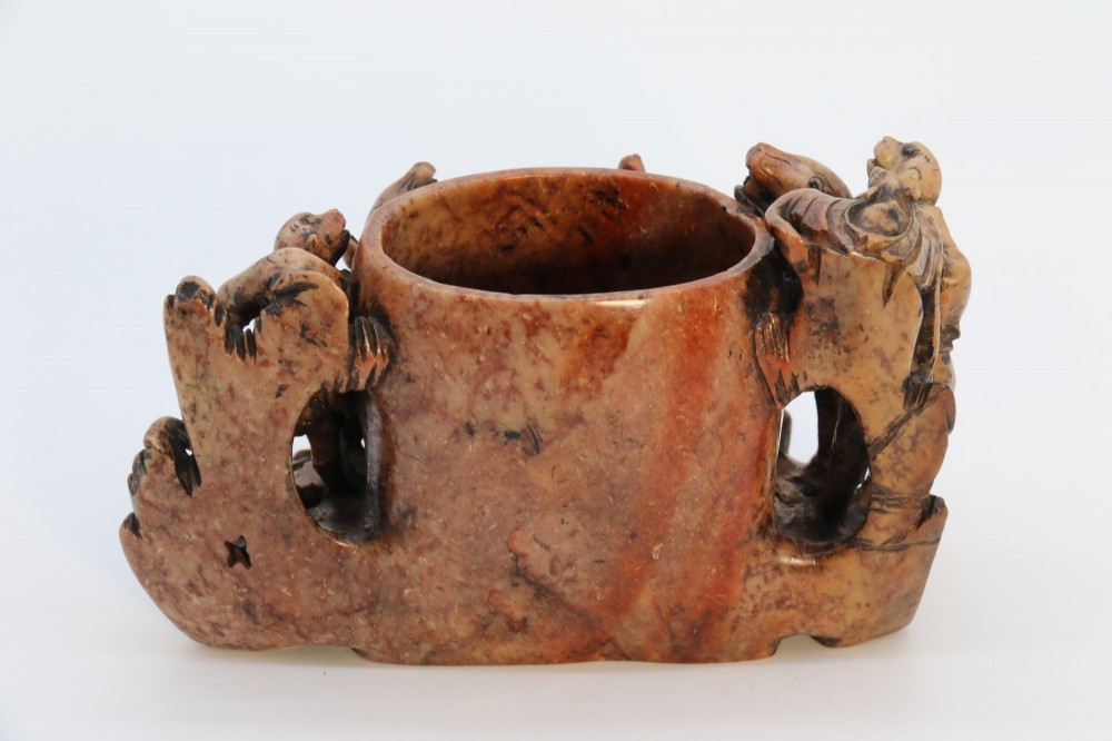 A cylindrical reddish-brown carved soapstone brush pot featuring sculpted animal figures in high relief surrounding an engraved vessel. View VII