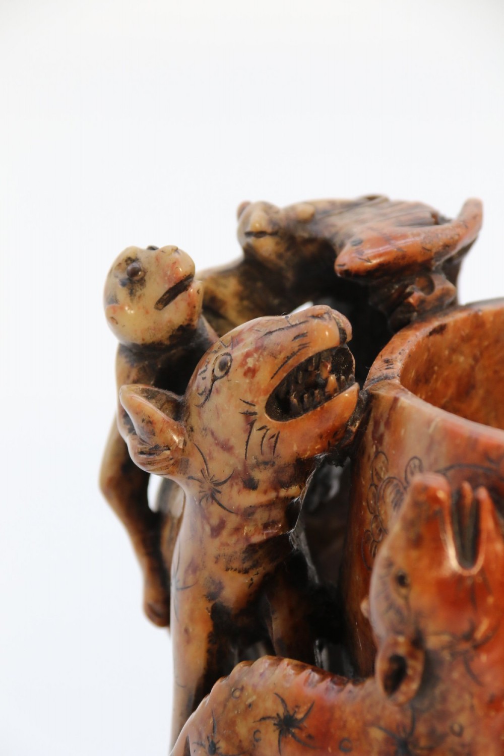 A cylindrical reddish-brown carved soapstone brush pot featuring sculpted animal figures in high relief surrounding an engraved vessel. View IX