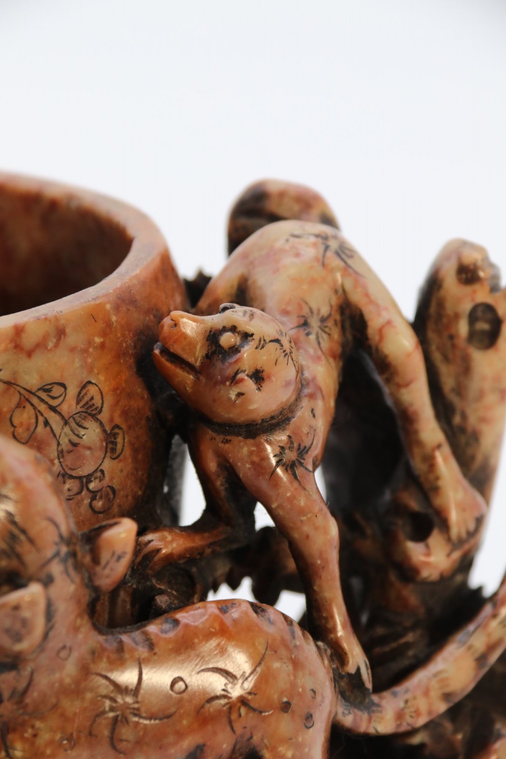 A cylindrical reddish-brown carved soapstone brush pot featuring sculpted animal figures in high relief surrounding an engraved vessel. View X