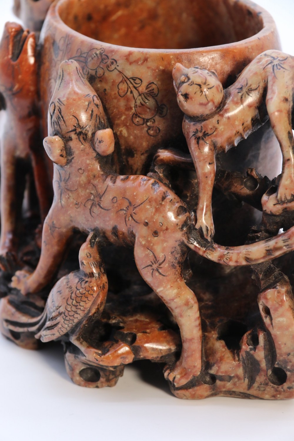 A cylindrical reddish-brown carved soapstone brush pot featuring sculpted animal figures in high relief surrounding an engraved vessel. View XII
