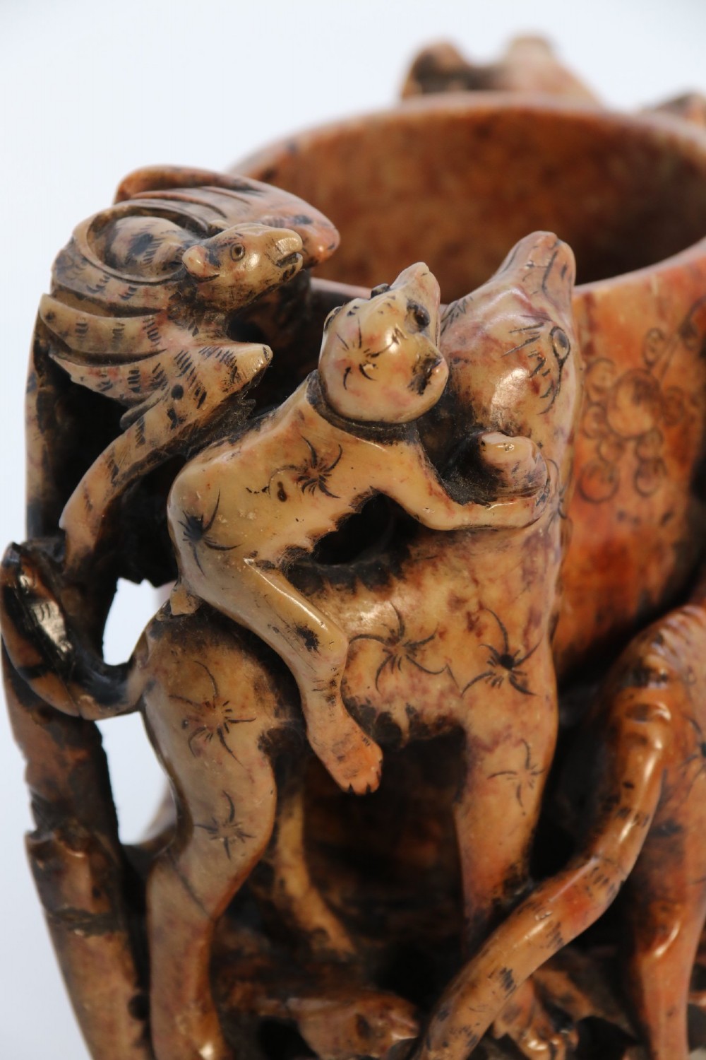 A cylindrical reddish-brown carved soapstone brush pot featuring sculpted animal figures in high relief surrounding an engraved vessel. View XIII