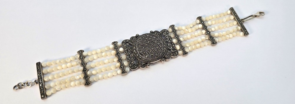 An Art Deco style multi-strand bracelet featuring white mother of pearl beads separated by intricate silver and marcasite decorative panels. View II