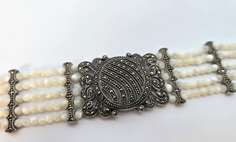 An Art Deco style multi-strand bracelet featuring white mother of pearl beads separated by intricate silver and marcasite decorative panels. View IV