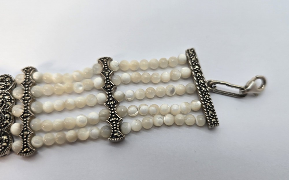 An Art Deco style multi-strand bracelet featuring white mother of pearl beads separated by intricate silver and marcasite decorative panels. View V