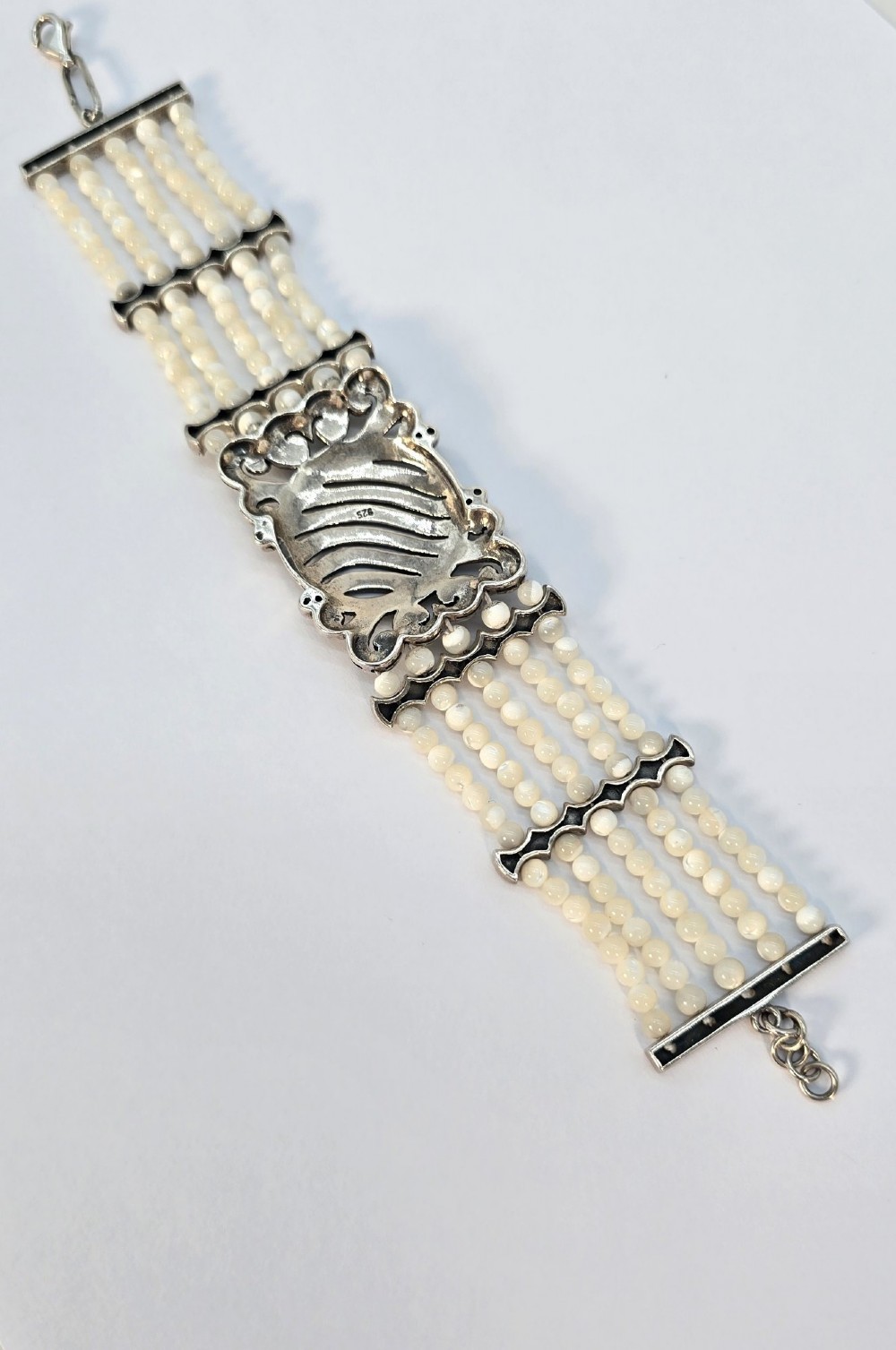 An Art Deco style multi-strand bracelet featuring white mother of pearl beads separated by intricate silver and marcasite decorative panels. View VII