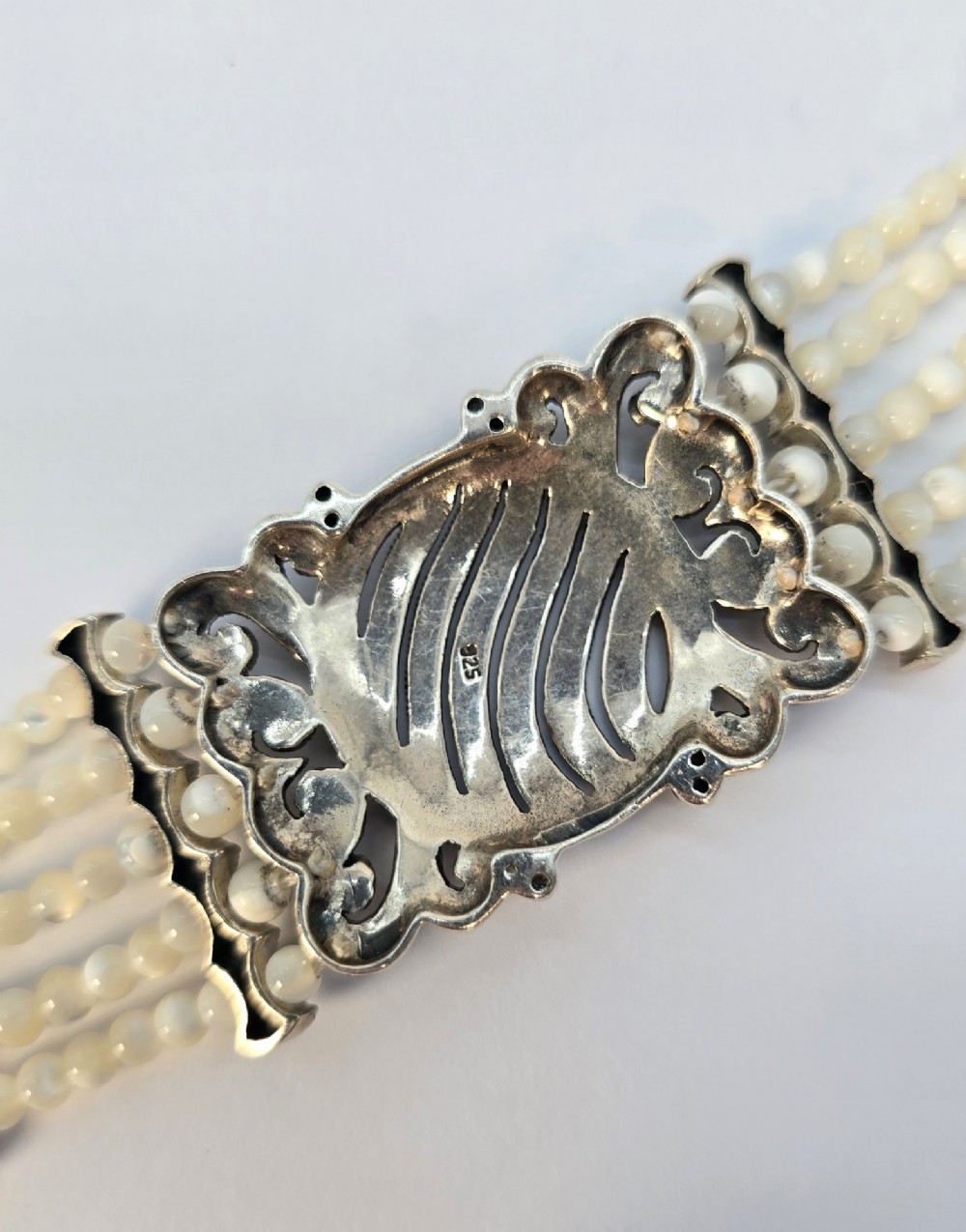 An Art Deco style multi-strand bracelet featuring white mother of pearl beads separated by intricate silver and marcasite decorative panels. View VIII