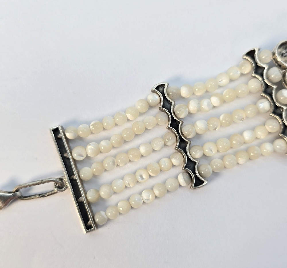 An Art Deco style multi-strand bracelet featuring white mother of pearl beads separated by intricate silver and marcasite decorative panels. View IX