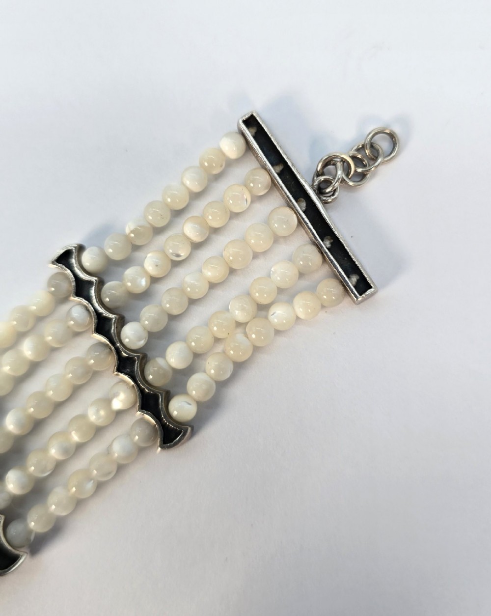 An Art Deco style multi-strand bracelet featuring white mother of pearl beads separated by intricate silver and marcasite decorative panels. View X