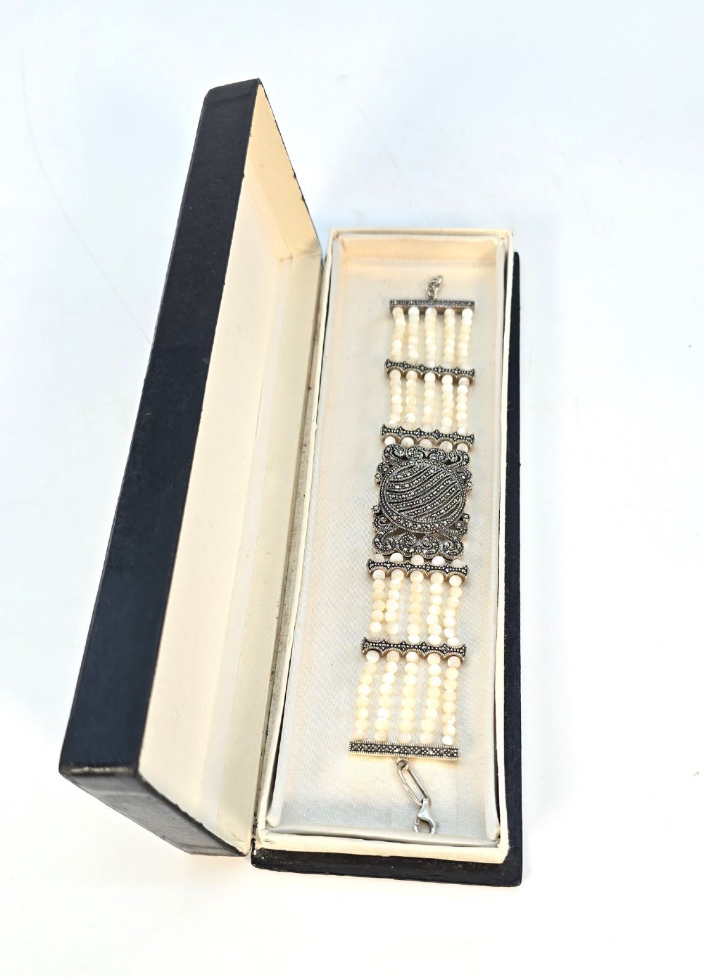 An Art Deco style multi-strand bracelet featuring white mother of pearl beads separated by intricate silver and marcasite decorative panels. View XI