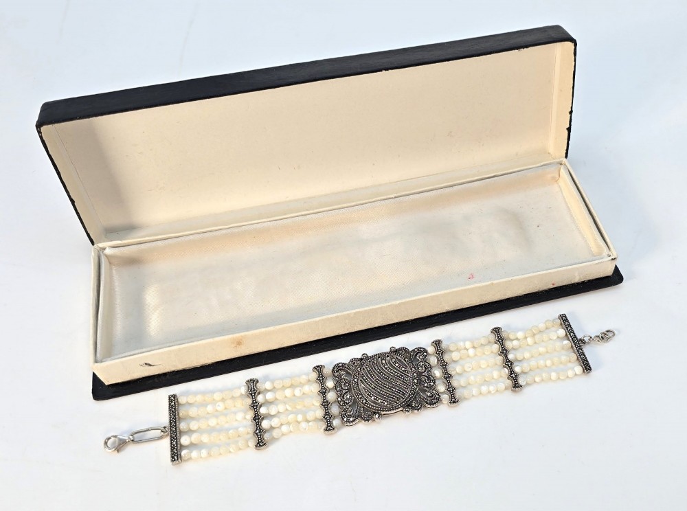 An Art Deco style multi-strand bracelet featuring white mother of pearl beads separated by intricate silver and marcasite decorative panels. View XII