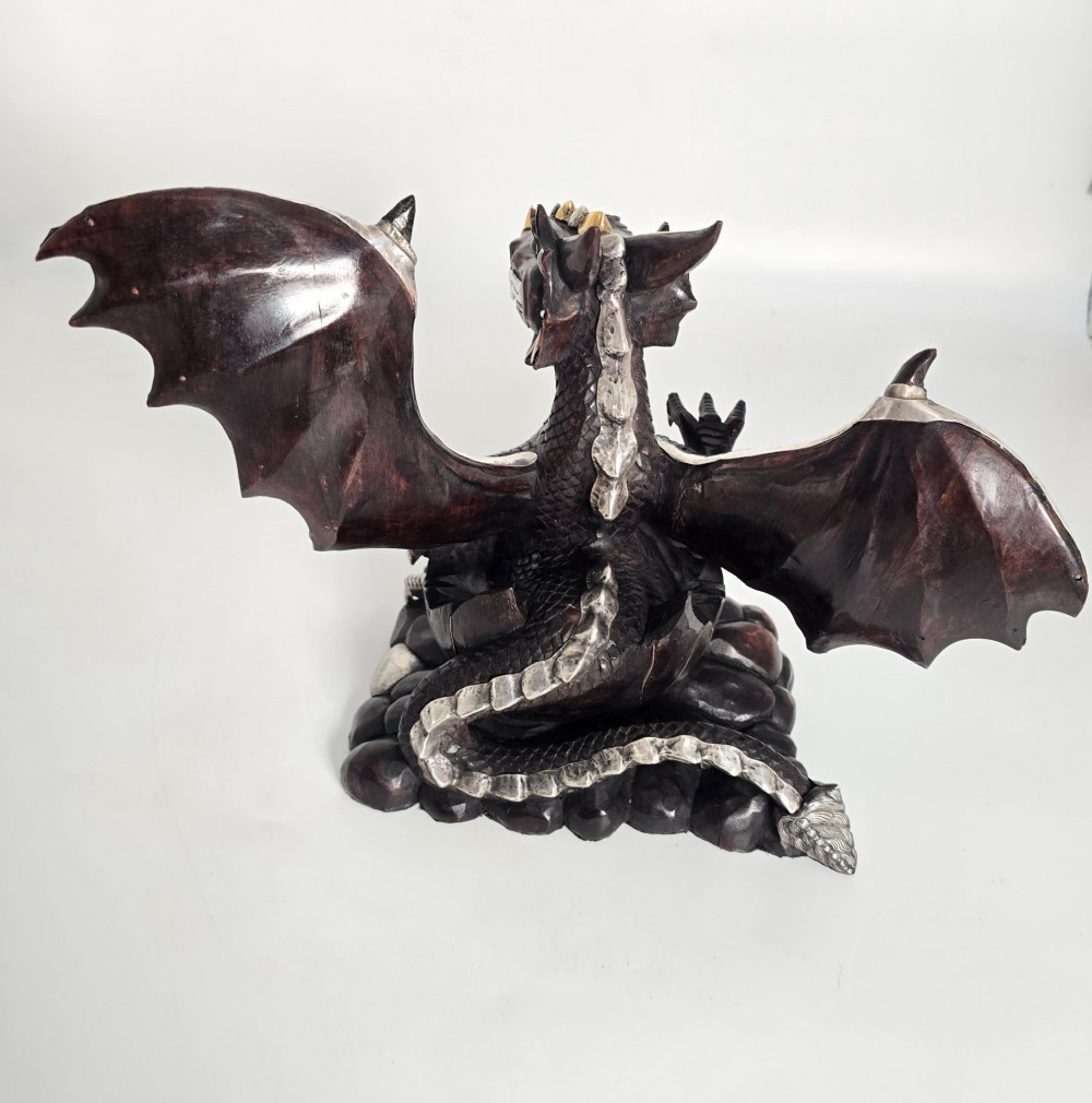 A carved dark hardwood sculpture depicting a dragon hatching from an egg, detailed with silvered and brass metal mounts on its wings, underbelly, and claws. View VII
