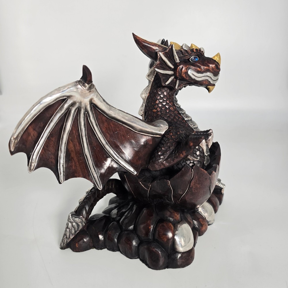 A carved dark hardwood sculpture depicting a dragon hatching from an egg, detailed with silvered and brass metal mounts on its wings, underbelly, and claws. View VIII
