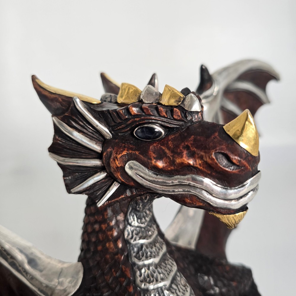 A carved dark hardwood sculpture depicting a dragon hatching from an egg, detailed with silvered and brass metal mounts on its wings, underbelly, and claws. View X