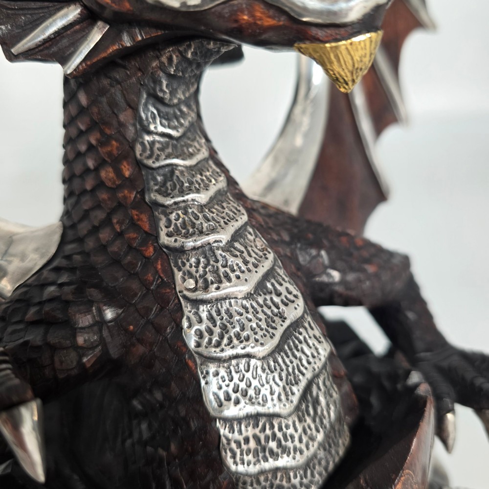 A carved dark hardwood sculpture depicting a dragon hatching from an egg, detailed with silvered and brass metal mounts on its wings, underbelly, and claws. View XI