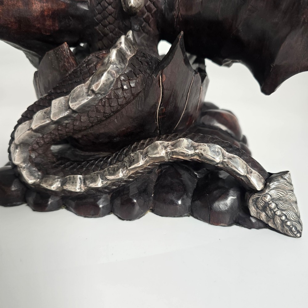 A carved dark hardwood sculpture depicting a dragon hatching from an egg, detailed with silvered and brass metal mounts on its wings, underbelly, and claws. View XII