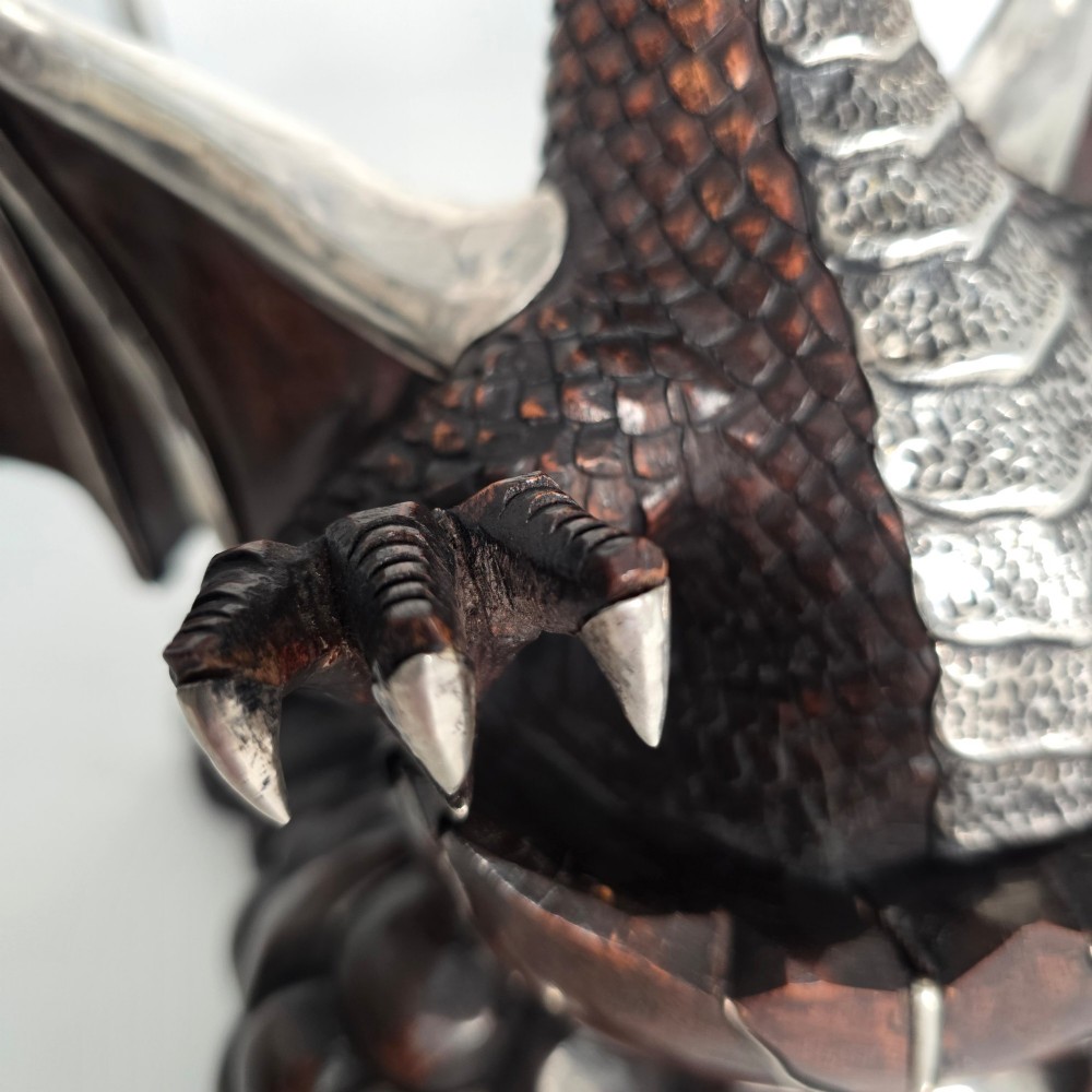 A carved dark hardwood sculpture depicting a dragon hatching from an egg, detailed with silvered and brass metal mounts on its wings, underbelly, and claws. View XIII