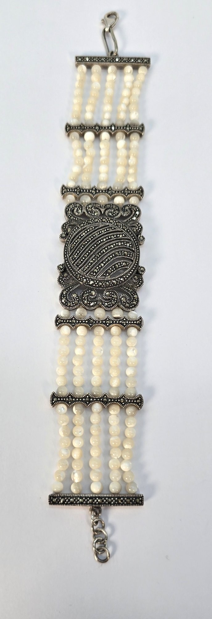 An Art Deco style multi-strand bracelet featuring white mother of pearl beads separated by intricate silver and marcasite decorative panels.