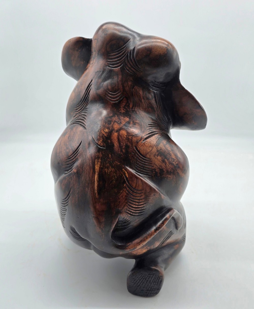 A dark carved hardwood sculpture of an elephant seated on its hind legs with its trunk raised and long tusks exposed. View VII