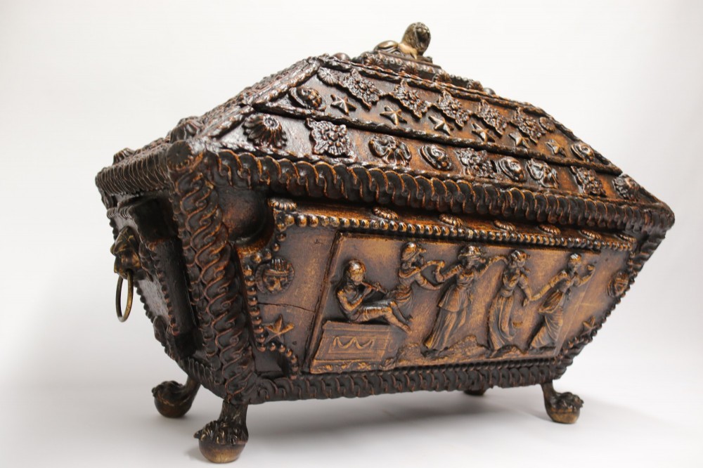 An early 19th-century sarcophagus-shaped gesso casket featuring raised classical relief panels, rope-twist borders, lion mask ring handles, and claw feet.