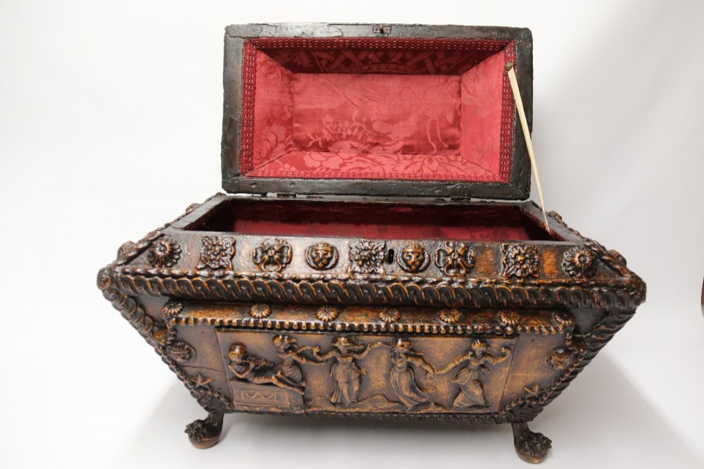 An early 19th-century sarcophagus-shaped gesso casket featuring raised classical relief panels, rope-twist borders, lion mask ring handles, and claw feet. View II