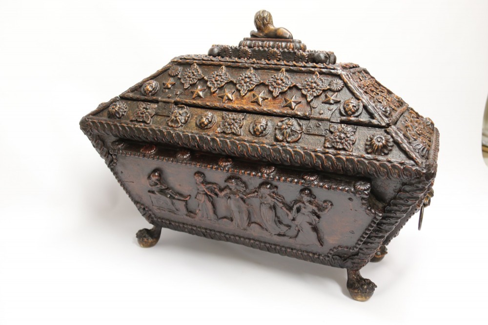 An early 19th-century sarcophagus-shaped gesso casket featuring raised classical relief panels, rope-twist borders, lion mask ring handles, and claw feet. View V