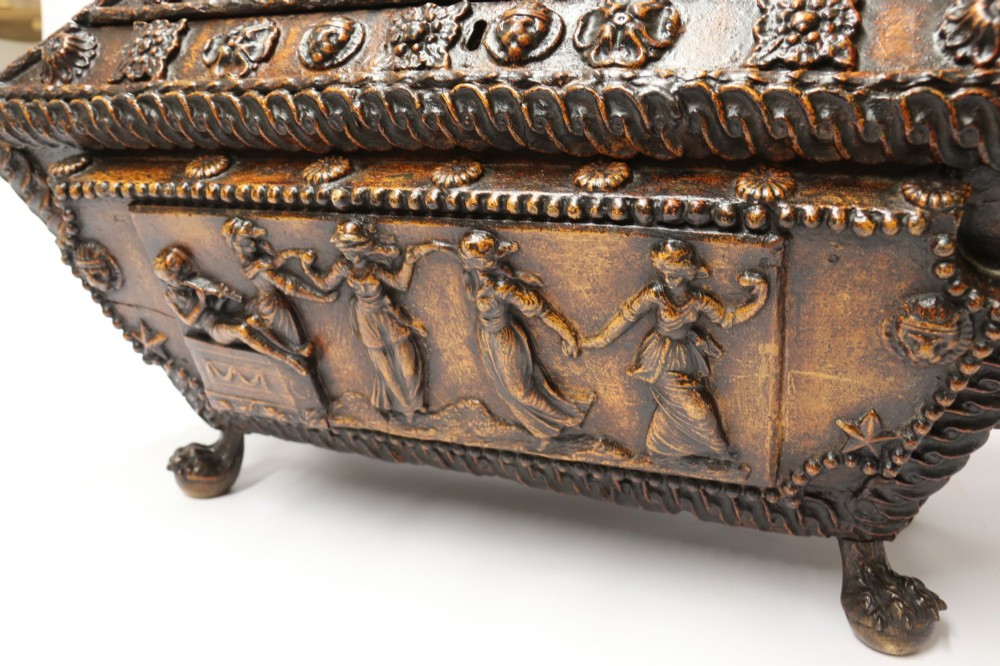 An early 19th-century sarcophagus-shaped gesso casket featuring raised classical relief panels, rope-twist borders, lion mask ring handles, and claw feet. View VI
