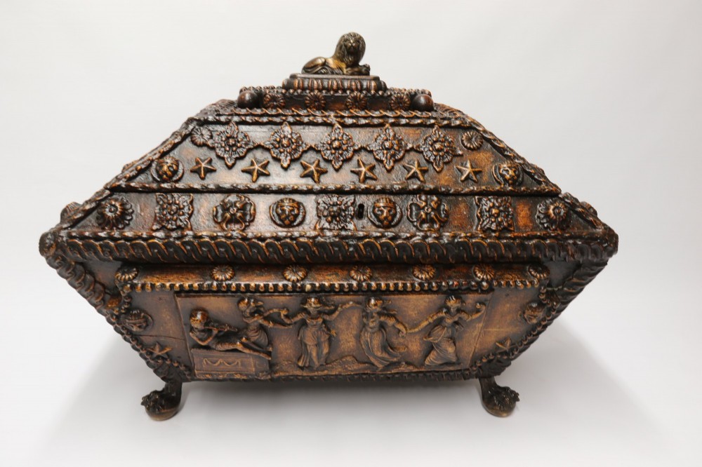 An early 19th-century sarcophagus-shaped gesso casket featuring raised classical relief panels, rope-twist borders, lion mask ring handles, and claw feet. View IX