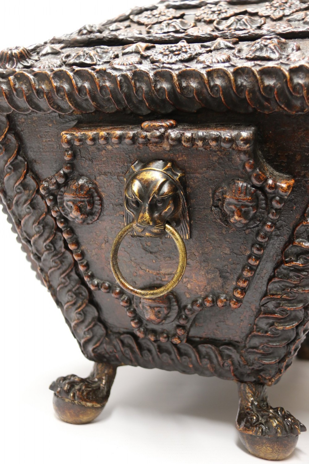 An early 19th-century sarcophagus-shaped gesso casket featuring raised classical relief panels, rope-twist borders, lion mask ring handles, and claw feet. View XII