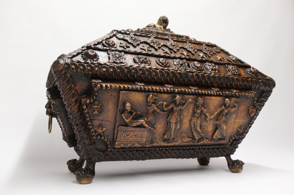 An early 19th-century sarcophagus-shaped gesso casket featuring raised classical relief panels, rope-twist borders, lion mask ring handles, and claw feet. View XIII