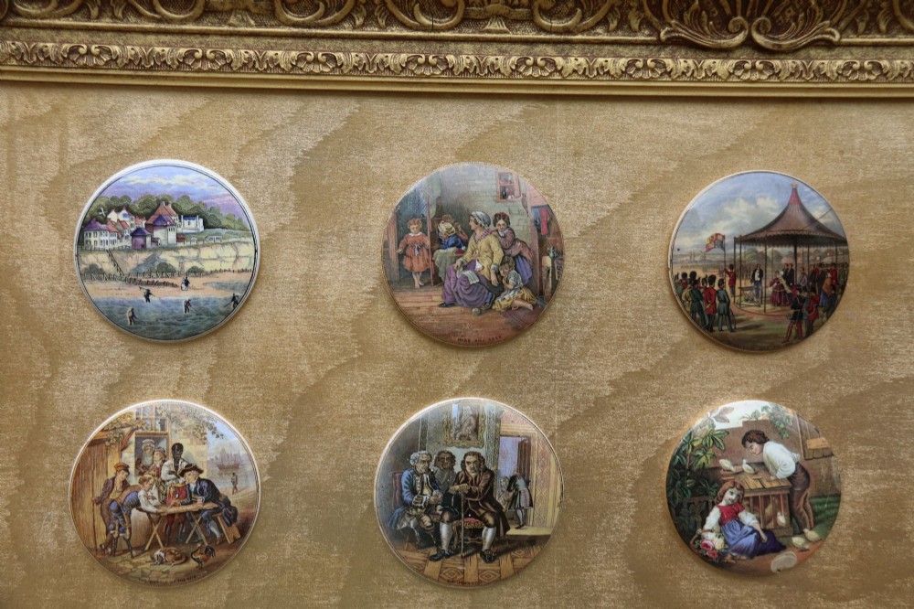 A large rectangular ornate gilt frame displaying thirty-five circular Victorian polychrome transfer-printed ceramic pot lids mounted in grid formation. View II