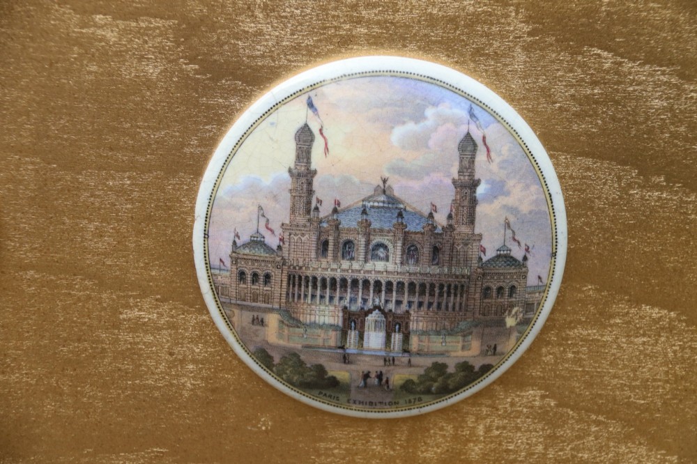 A large rectangular ornate gilt frame displaying thirty-five circular Victorian polychrome transfer-printed ceramic pot lids mounted in grid formation. View XV