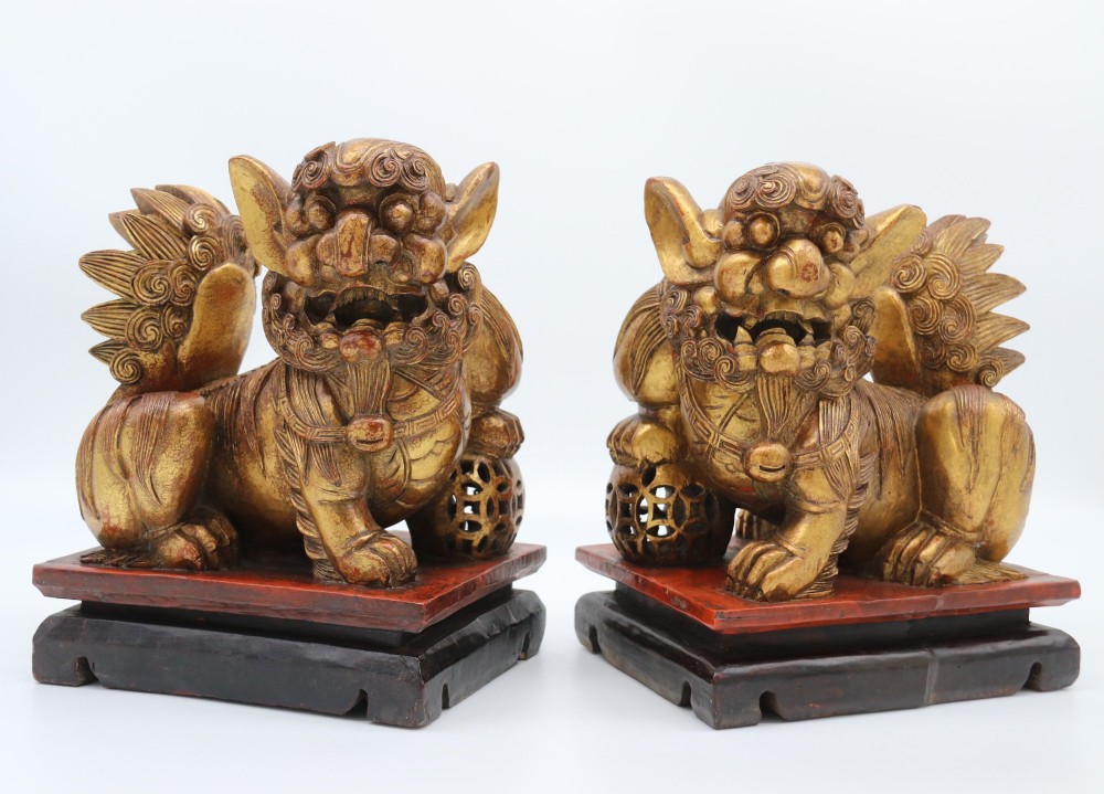 A pair of hand-carved Chinese wooden guardian lions finished in gold gilding and red lacquer, seated on dark rectangular bases.