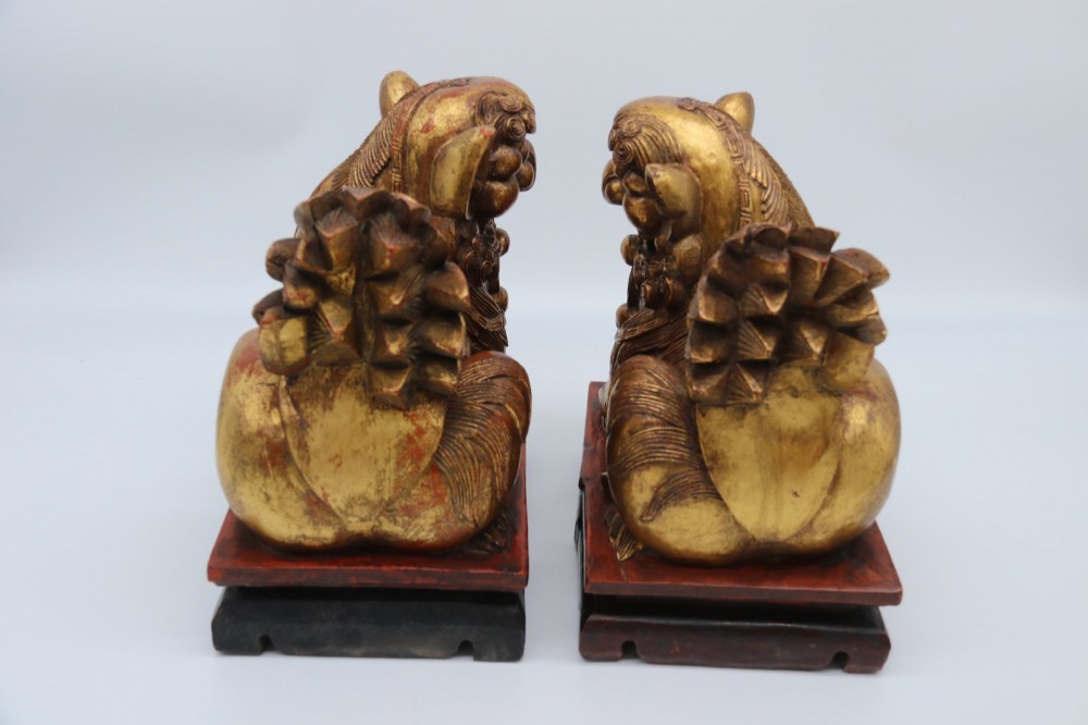 A pair of hand-carved Chinese wooden guardian lions finished in gold gilding and red lacquer, seated on dark rectangular bases. View II
