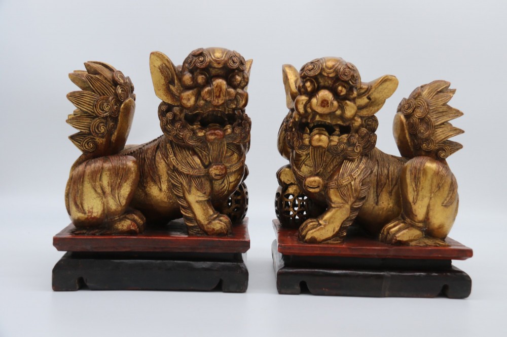 A pair of hand-carved Chinese wooden guardian lions finished in gold gilding and red lacquer, seated on dark rectangular bases. View IV