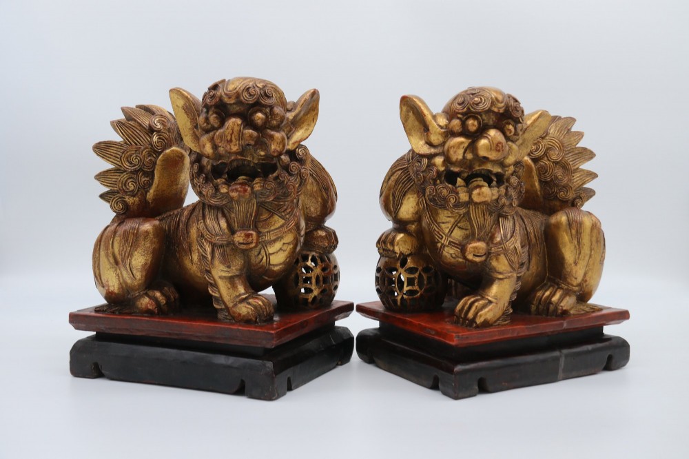 A pair of hand-carved Chinese wooden guardian lions finished in gold gilding and red lacquer, seated on dark rectangular bases. View V